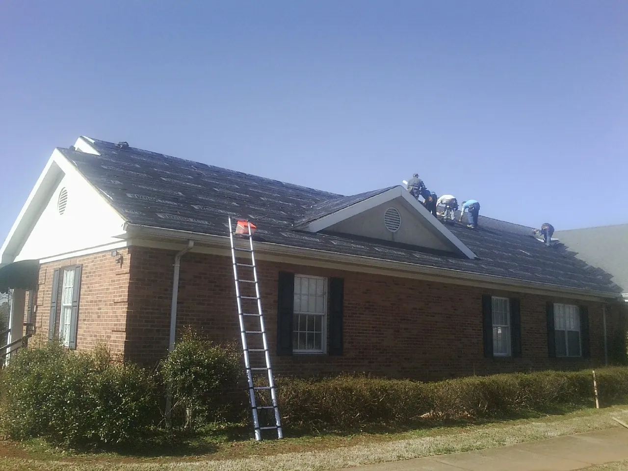 Crew tearing shingles off a brick ranch roof with a ladder set — Metal Roof Repair work by our crew in McCall