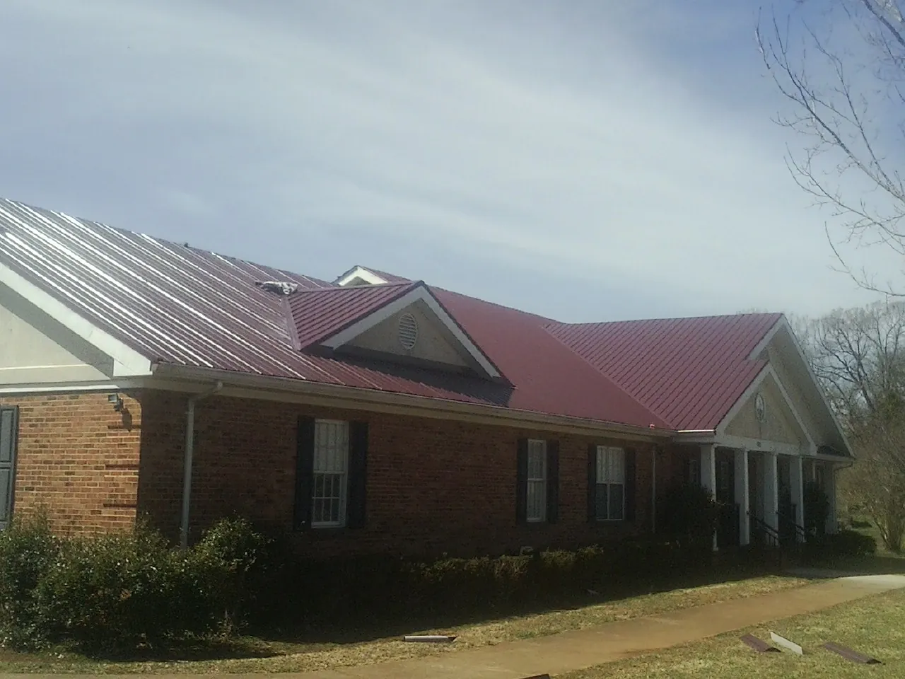 Red metal roof with gabled entries on a long brick building, from a Hail Damage Roof Repair job in McCall