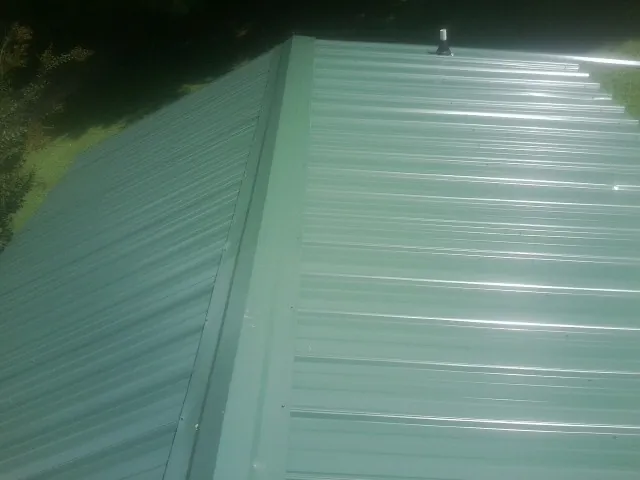 New green metal panels meeting at the ridge of a roof — Flat Roof Repair work by our crew in McCall
