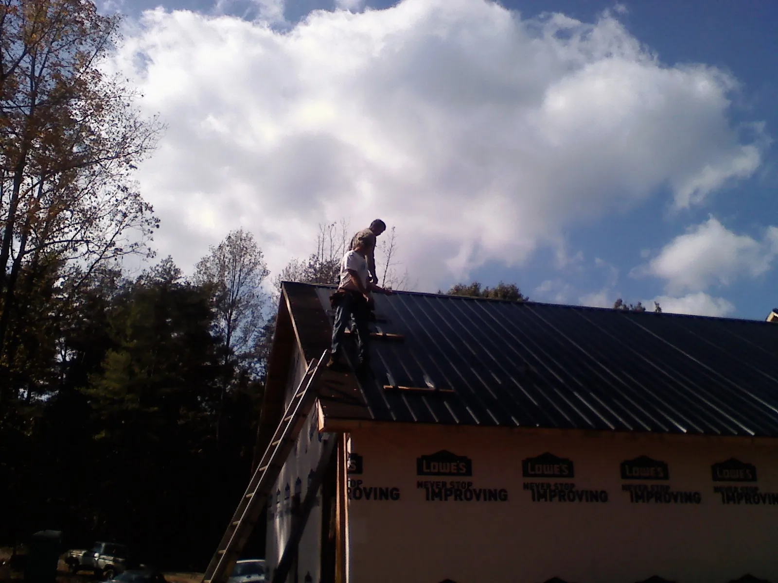 Roofer fastening dark metal panels high against a cloudy sky, from a Roof Inspection job in McCall